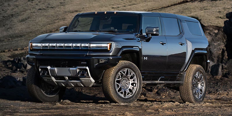 A dark gray Hummer EV SUV parked on a rocky, brown landscape with a slight incline.