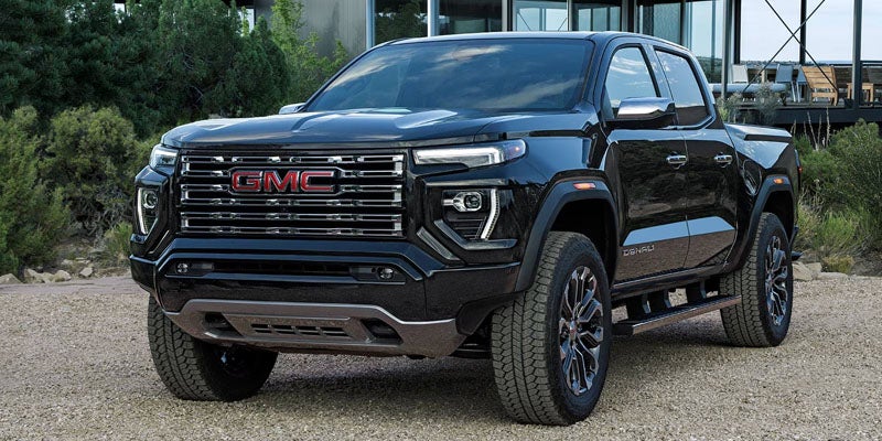 Black GMC Denali pickup truck with chrome grille and red emblem, parked on a gravel path.