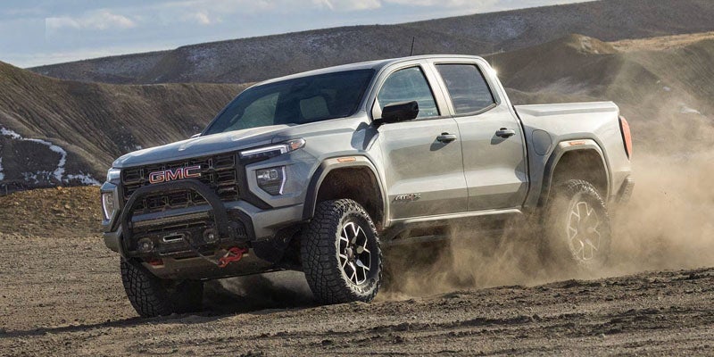 Light gray GMC Canyon truck kicks up dust as it drives over undulating terrain.