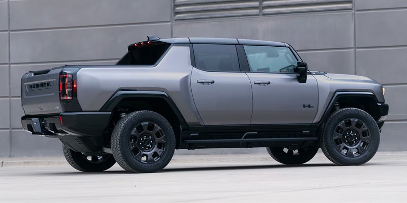 Rear three-quarter view of a gray Hummer EV pickup truck with black trim, wheels, and bed cover.