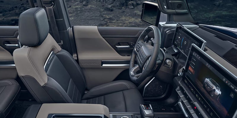View of a modern car interior showing a two-tone seat, steering wheel, and digital infotainment screens.