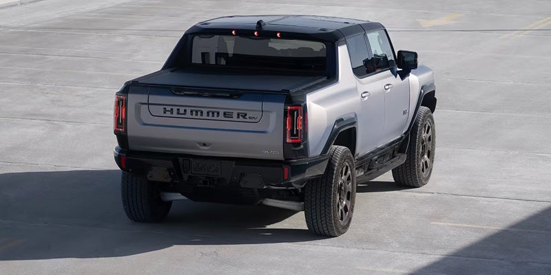 Rear view of a silver Hummer EV truck with a black cargo bed cover on a concrete lot.