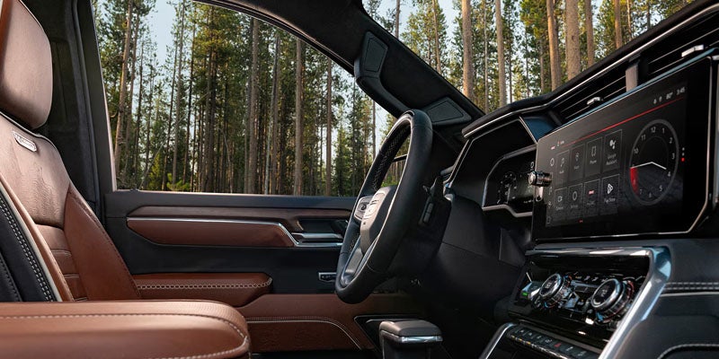 Spacious brown leather car interior with a large touchscreen infotainment system and a forest visible through the windows.