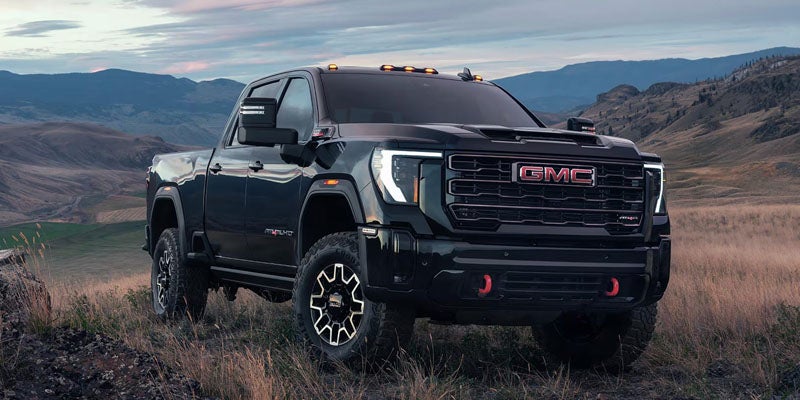 A black GMC Sierra AT4X truck with red tow hooks parked on a grassy hill overlooking a valley at dusk.
