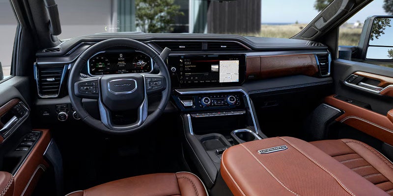 Interior of a GMC Denali Ultimate truck, featuring brown leather seats, dark wood trim, and multiple digital displays.