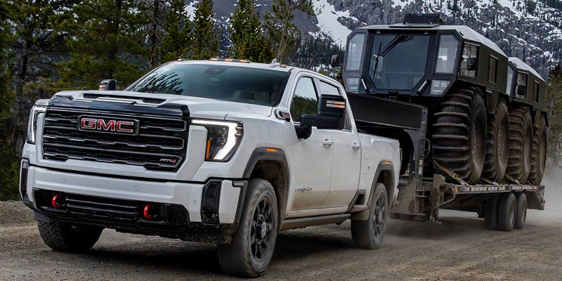 A red GMC Sierra AT4X pickup truck angled on a rocky trail with trees and a mountain in the background.