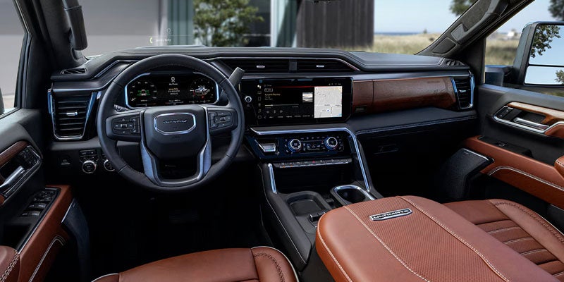 Spacious brown leather car interior with a large touchscreen infotainment system and a forest visible through the windows.