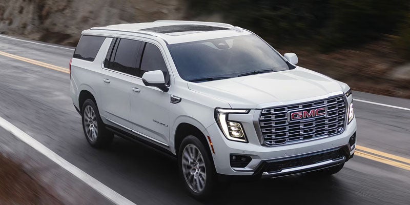 A white GMC Yukon Denali SUV driving on a highway with a mountain in the background.