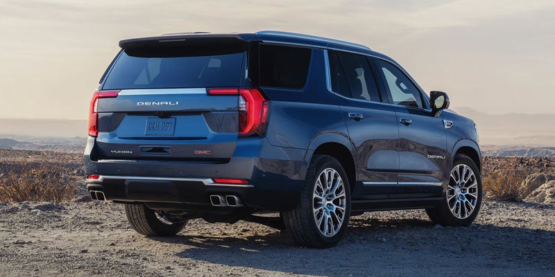 Rear view of a dark blue GMC Yukon Denali SUV parked on a dusty, rocky hill.