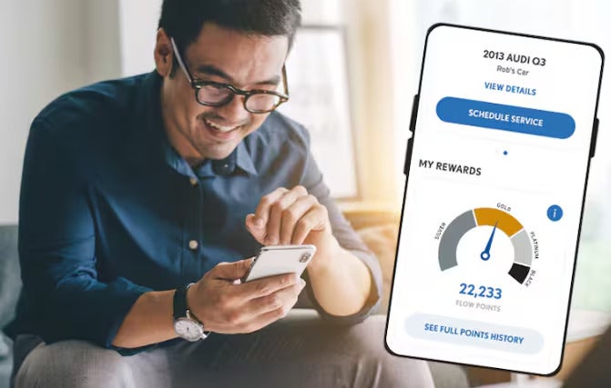 Smiling man in glasses looking at his phone, using a car service and rewards app.